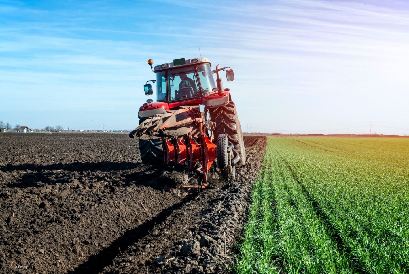 Un tracteur rouge labourant un champ avec un ciel bleu en arrière-plan.