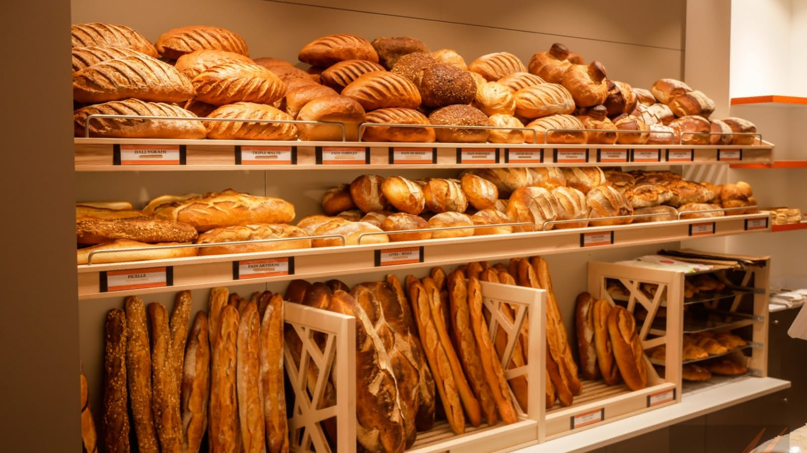 Un étal de boulangerie avec plusieurs paniers de pains variés, y compris des baguettes et des pains ronds, disposés sur des étagères.