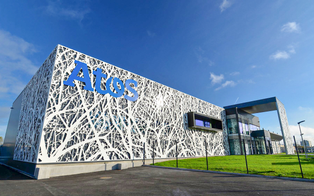 Image du bâtiment moderne d'Atos avec une façade blanche et des motifs complexes, situé dans un environnement urbain lumineux.