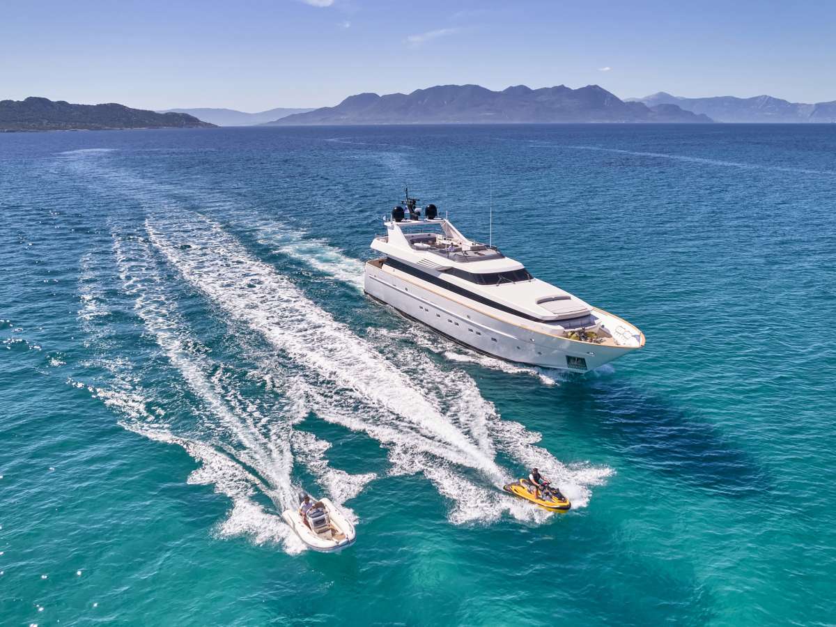 Un yacht luxueux naviguant sur des eaux turquoise, accompagné de deux petites embarcations à moteur.