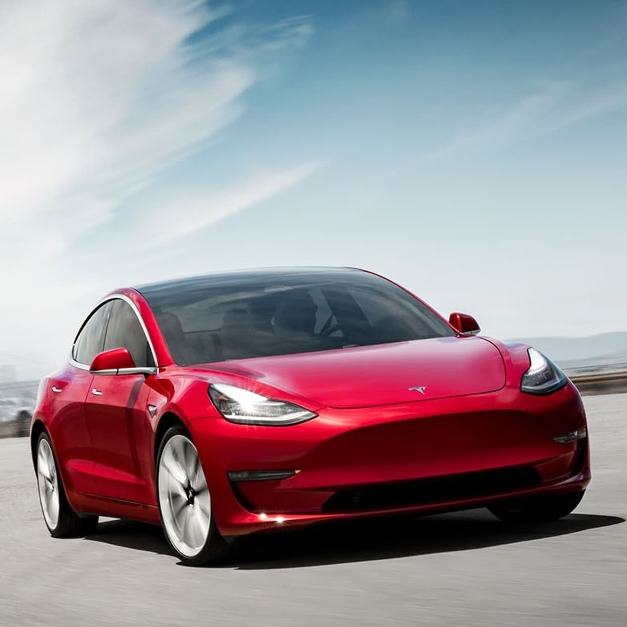 Voiture électrique rouge en mouvement sur une route avec un ciel bleu en arrière-plan.